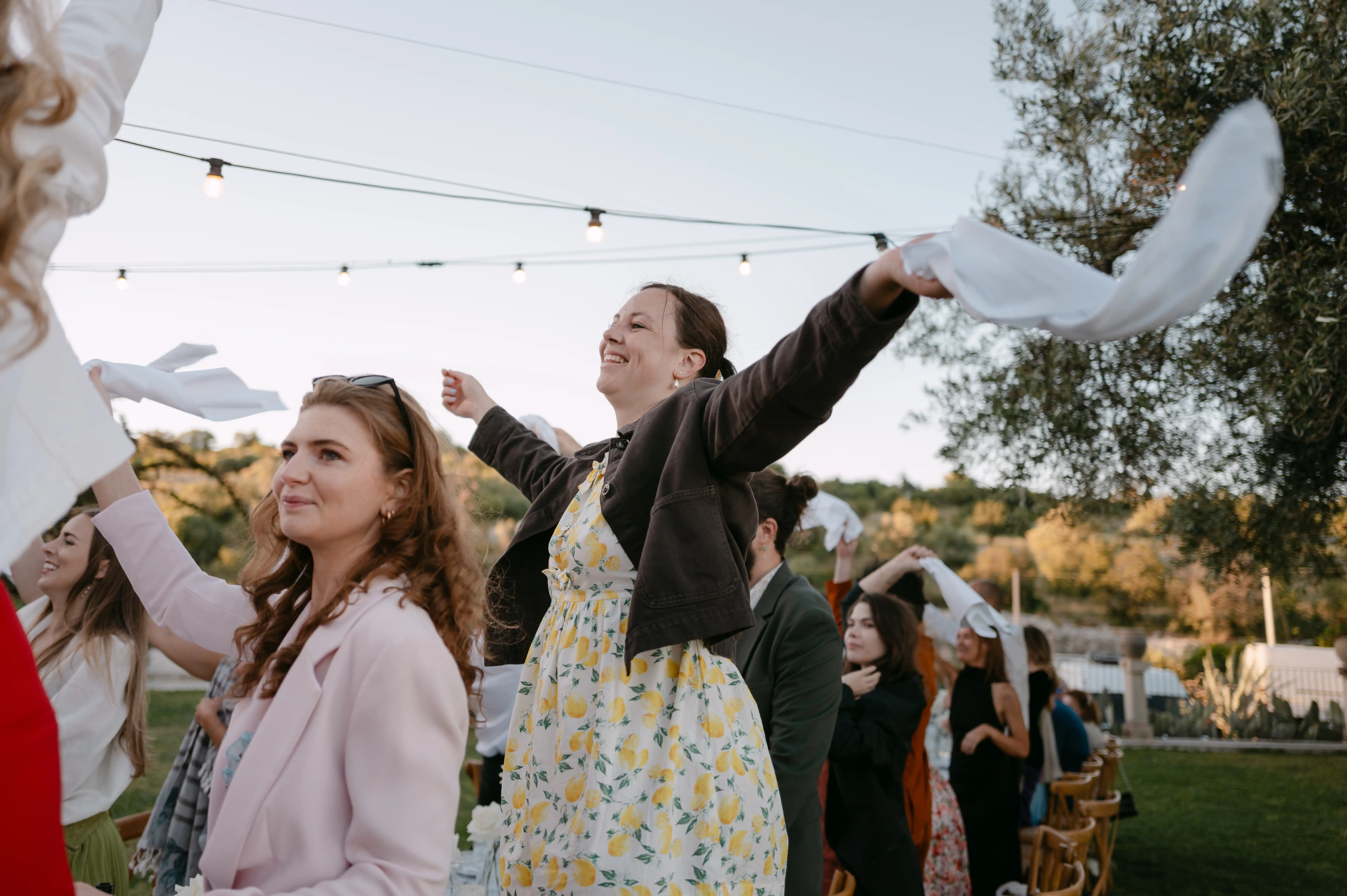 Wedding guests dancing and waving napkins beside long reception tables at a romantic destination wedding in Italy.